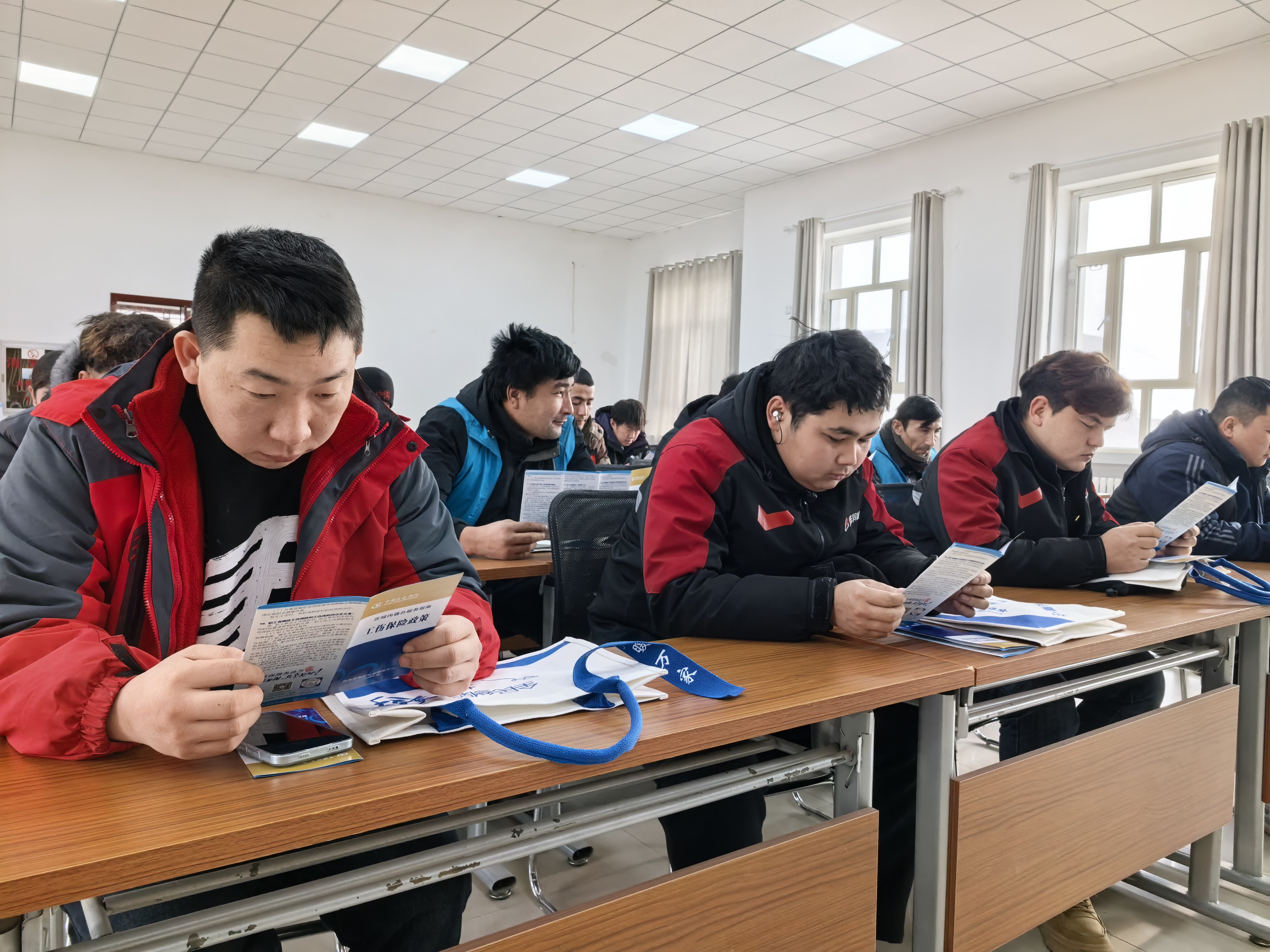 12月24日，沙雅县人社局社保中心联合县委社会工作部举办“外卖快递跑万家 社保护航你我他”政策宣讲会。图为骑手正在认真阅读社会保险区域通办服务指南。.jpg